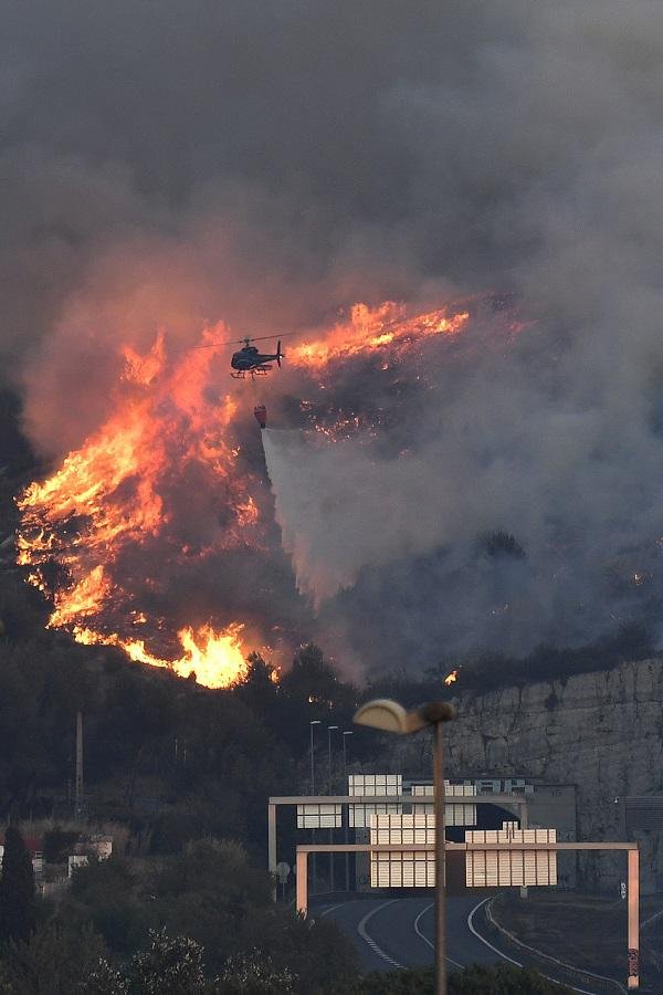 Un hélicoptère survole les flammes qui bordent l'autoroute