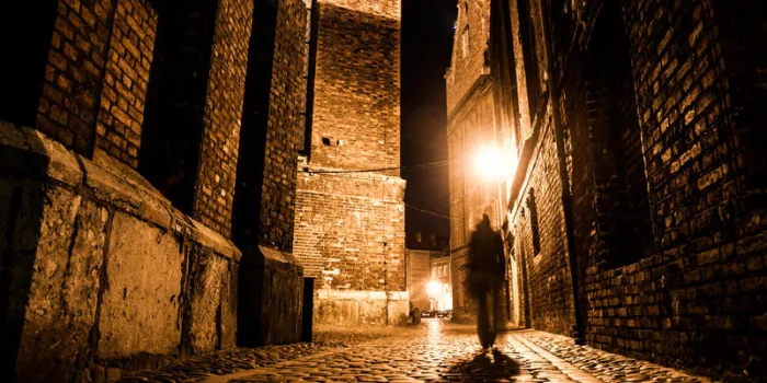 rue pavée illuminée avec des reflets lumineux sur les pavés dans la vieille ville historique de nuit silhouette floue sombre de la personne évoque jack l'éventreur