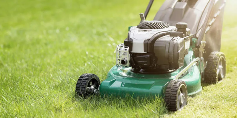 tondre ou couper l'herbe longue avec une tondeuse à gazon verte au soleil d'été