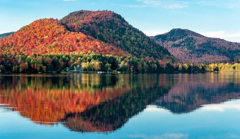les collines couvertes de forêts d'érables rouges se reflètent dans un lac au québec lors d'une belle soirée d'automne