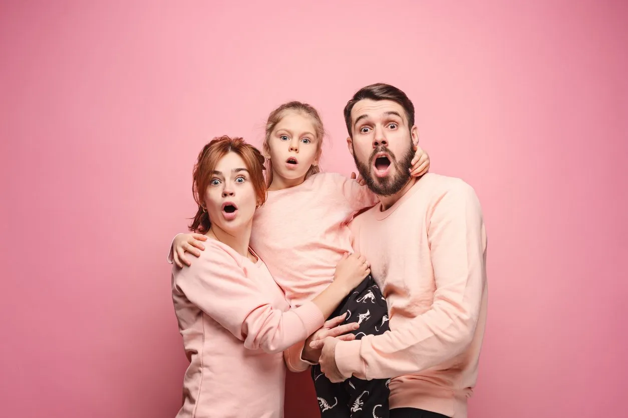 surprised young family looking at camera on pink studio background