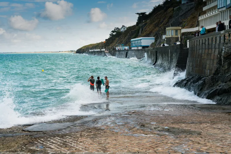 granville, manche   france - 18 august, 2019  three free divers preparing to jump into stormy ocean waters