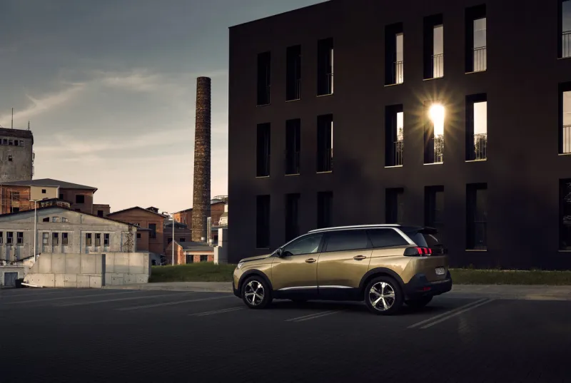 katowice poland - 06032017  golden peugeot 5008, seven-person suv, in the parking lot under a modern black office building porcelana slaska park in the back you can see the old factory buildings