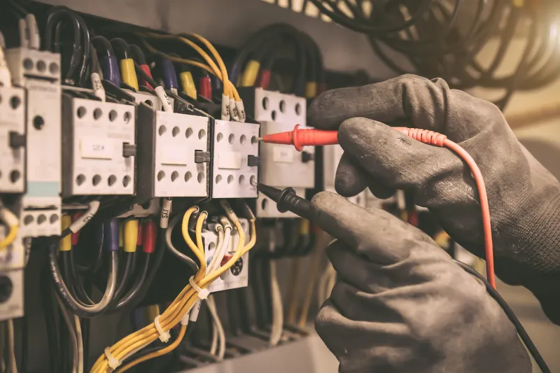 electrical engineer using digital multi-meter to check current voltage at circuit breaker in main distribution board