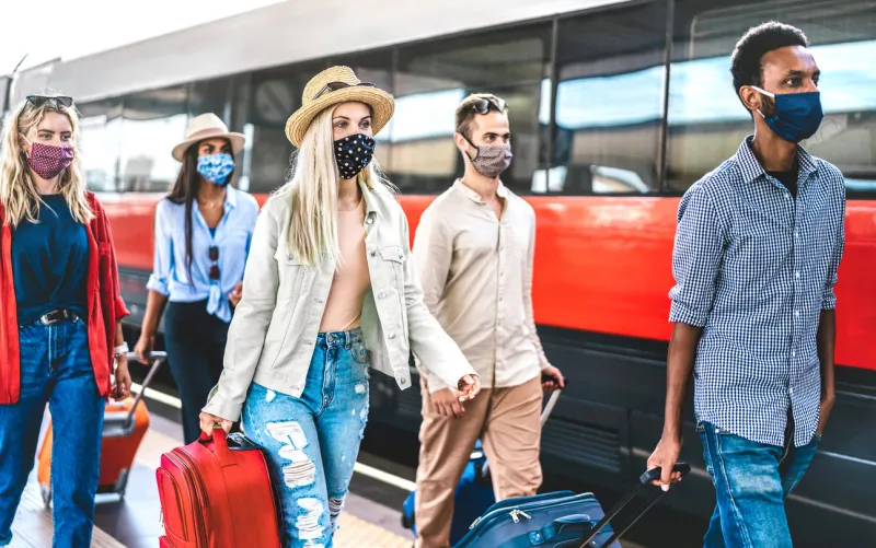 multiracial friends group walking at railway station platform - new normal travel concept with young travelers on social distancing and face covered by protective mask - focus on blonde girl with hat