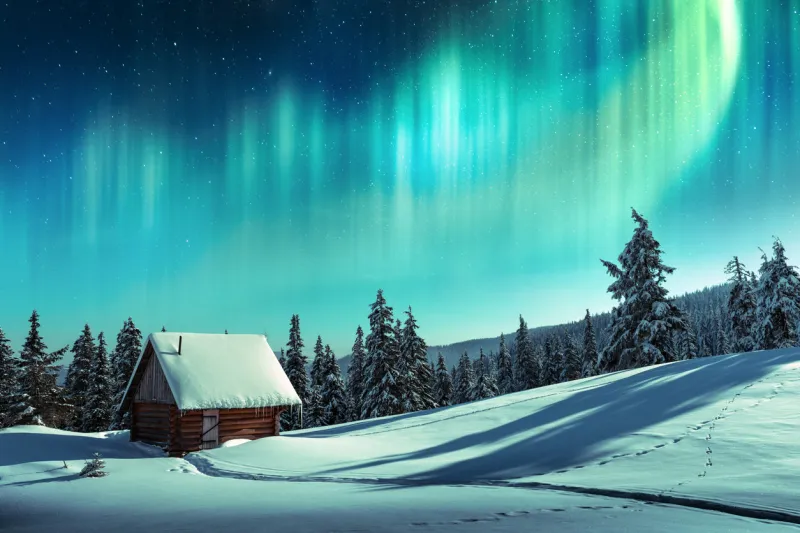 fantastic winter landscape with wooden house in snowy mountains and northen light in night sky