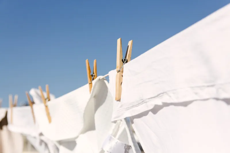 white clothes hung out to dry on a washing line in the bright warm sun background is a clear blue sky