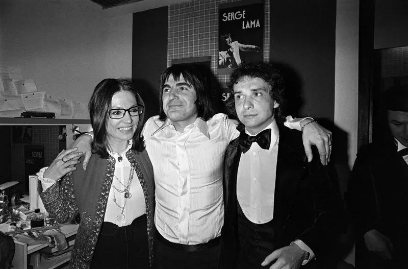 la chanteuse grecque nana mouskouri (g) et le chanteur michel sardou (d) félicitent le chanteur serge lama à l'issue de sa prestation sur la scène du palais des congrès de la porte maillot, à paris, le 12 janvier 1977  afp photo (photo by -   afp)