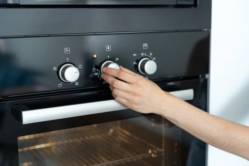 cropped view of woman select program turning switch at modern built in oven, select program, standing in kitchen
