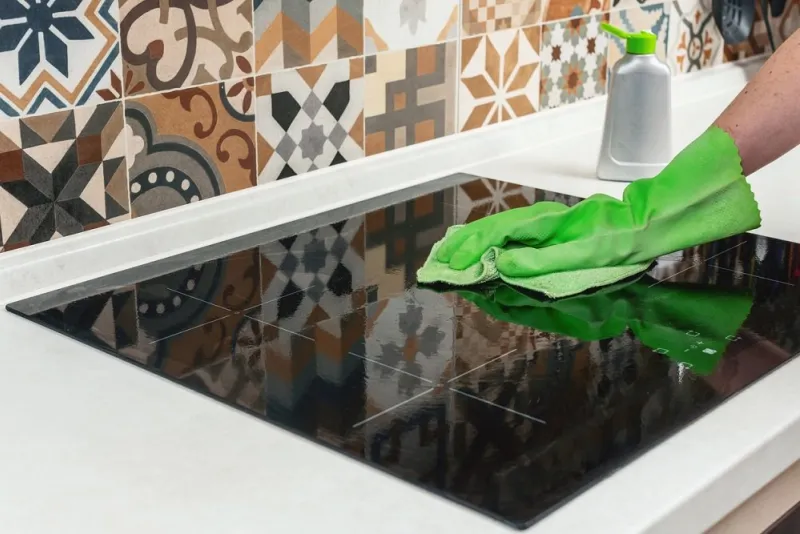 young woman hand cleaning a modern black induction hob by a rag, housework cleaning ceramic glass cooktop