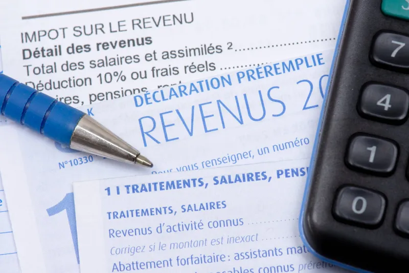 french pre-filled income tax return with the page about income from salaries, treatments, pensions and annuities, along with a pen and a calculator
