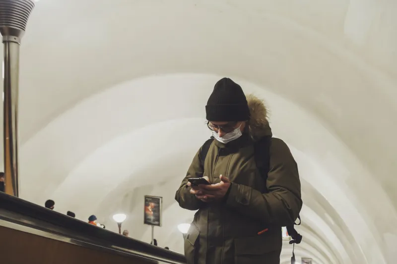 young man in wear casual winter clothes with glasses and medical mask at metro escalator attractive teenager with phone in big city subway, looking at mobile phone and emotions of an unexpected email