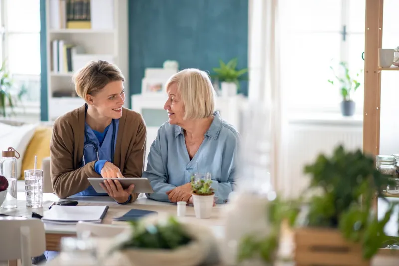 caregiver or healthcare worker with senior woman patient, using a tablet and explaining