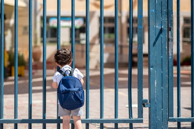 kid with school backpack look on schoolyard towards an open entrance or exit door schools and preschools remain locked for children during lockdown, coronavirus pandemic and second wave of covid-19