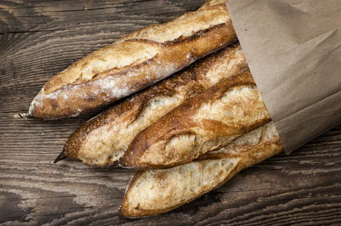 four baguette bread loaves in paper bag on wooden background