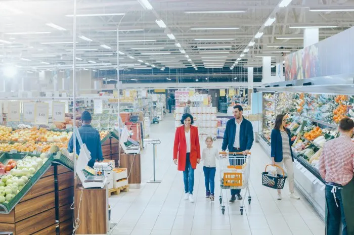 at the supermarket  happy family of three, holding hands, walks through fresh produce section of the store father, mother and daughter having fun time shopping high angle panoramic shot