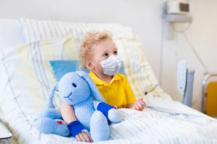 little boy playing wearing face mask with his toy in bed in hospital room child with iv tube and pulse oximeter in clinic kid recovering from coronavirus corona virus outbreak patient in kids ward