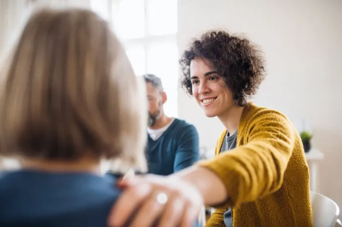 serious men and women sitting in a circle during group therapy, supporting each other