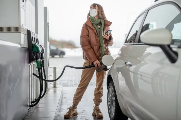 woman in face mask refueling car with a gasoline, using smartphone to pay concept of mobile technology for fast refueling without visiting the store