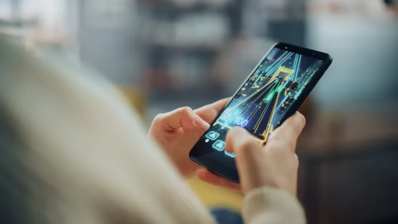 close up on a person hands playing an arcade video game on a vertically held smartphone at home living room feminine hands tapping the mobile phone screen with a colorful game over the internet