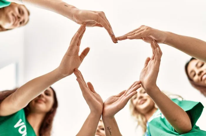 group of young volunteers woman smiling happy make heart symbol with hands together at charity center