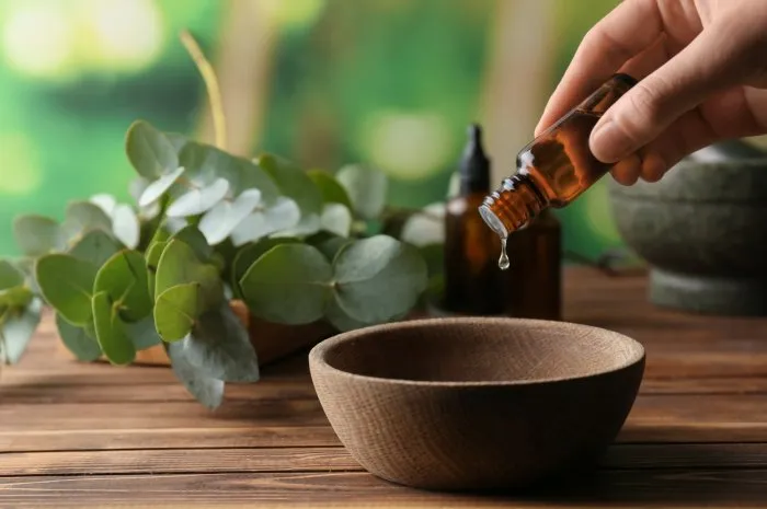 woman pouring eucalyptus essential oil into bowl on wooden table