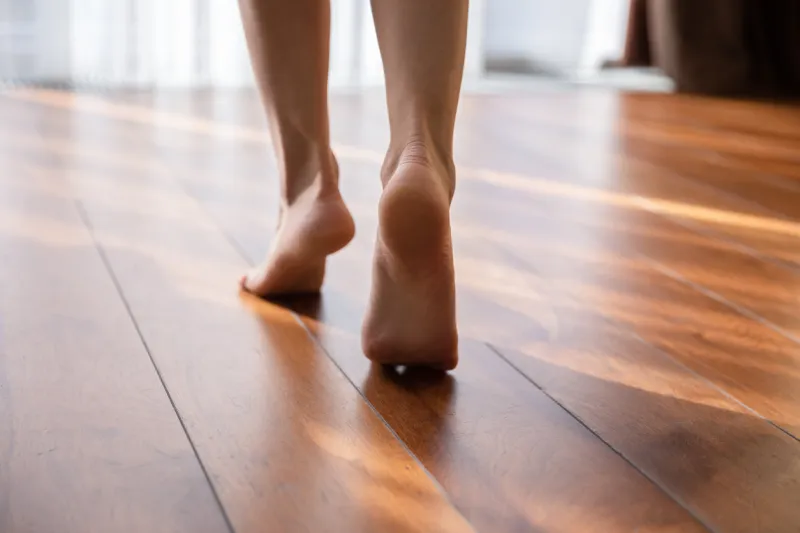 woman walking barefoot on toes at warm laminate floor close up rear view sunny light bedroom good morning welcome new day, modern comfy apartments with under floor heating system, footcare concept