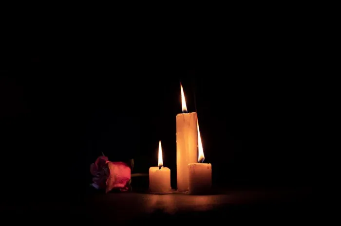 three lighted candles next to a rose on a black background
