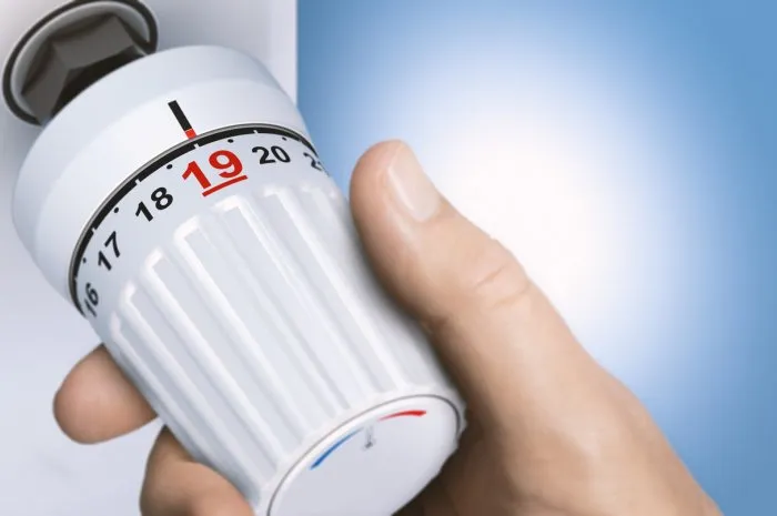 man reducing energy consumption by setting thermostat temperature to 19 degrees close up on a knob composite image between a 3d illustration and a hand photography
