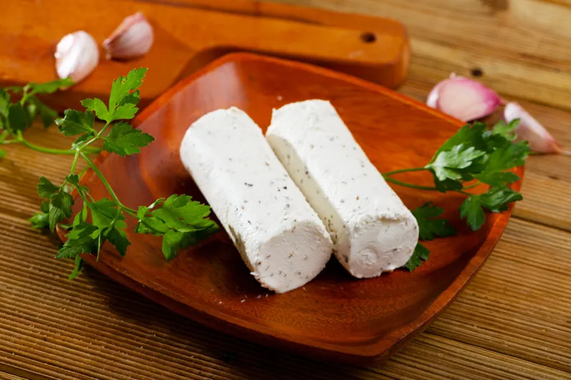 log-shaped fresh goat-milk cheese with herbs on plate on wooden surface