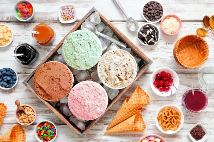 summer ice cream buffet with a variety of ice cream flavors and sweet toppings overhead view table scene on a rustic white wood background