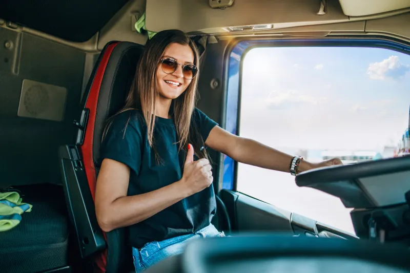 portrait of beautiful young woman professional truck driver sitting and driving big truck inside of vehicle people and transportation concept