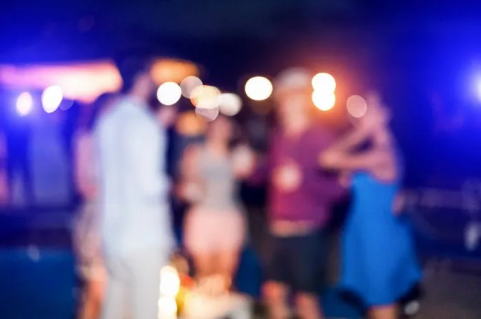 blurred people having sunset beach party in summer vacation - defocused image - concept of nightlife with cocktails and music entertainment - warm filter with blurry bokeh