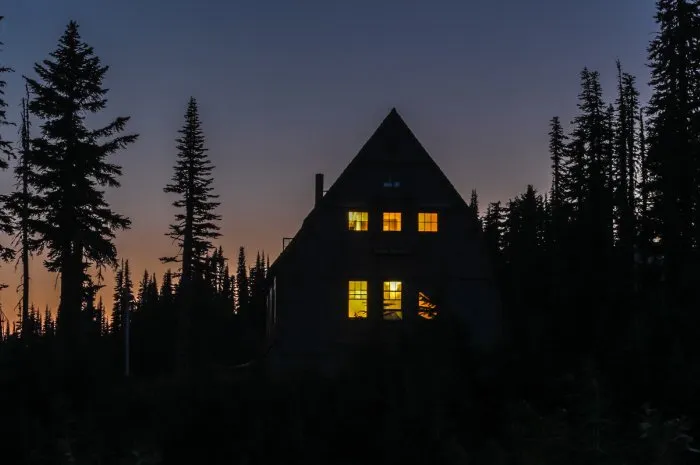 wooden cabin in the woods at night, windows are lit