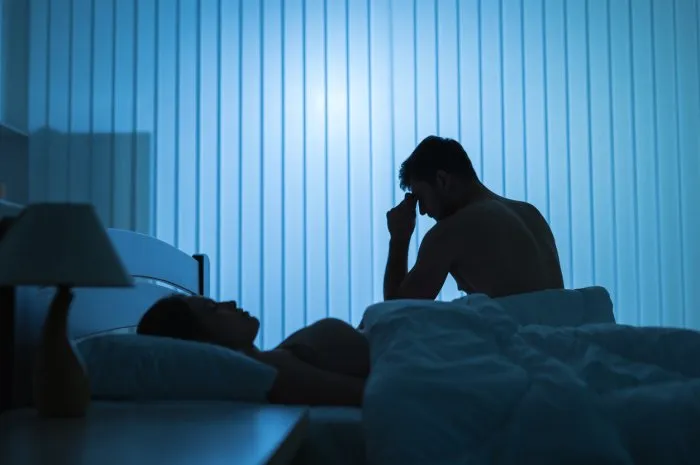 the worried man sit near near sleeping woman in the bed night time