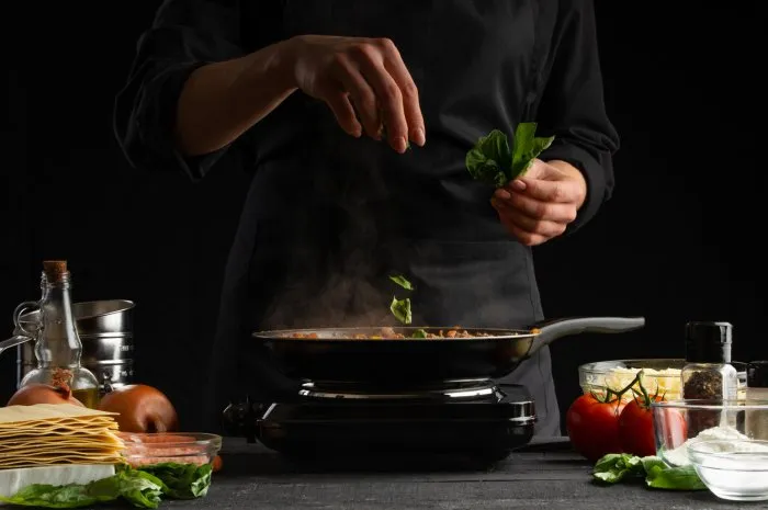 cooking by a chef italian lasagna, frying a dressing in a frying pan and sprinkling with basil freezing in motion cooking, homemade recipe book delicious and healthy food