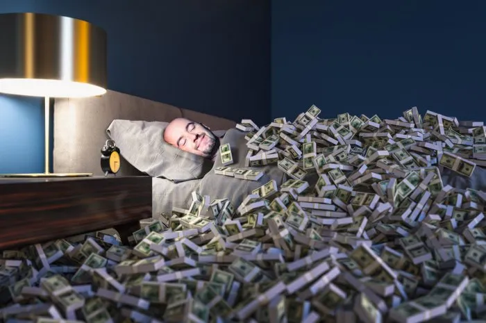 smiling man sleeping in a bed covered with dollars money wealth concept