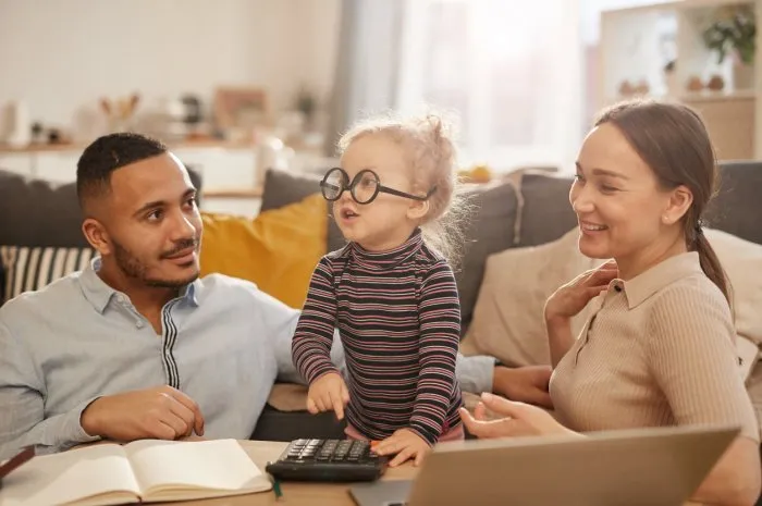 portrait of happy young family counting home finances with cute little girl wearing glasses in sunlit apartment