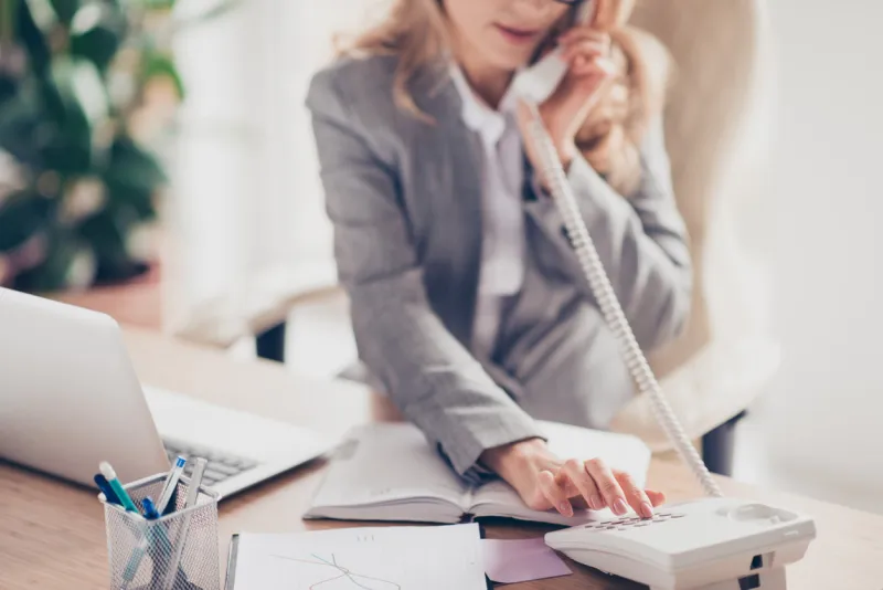 cropped closeup photo of clever smart professional polite secretary in grey formal suit is calling to her boss, she is sitting at the table in office