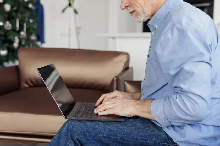 senior man reading online news, sending text messages on computer, working remotely from his home office cropped view of self-employed pensioner using modern laptop