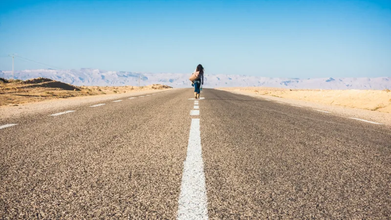 woman walking down middle of highway with a few belongings
