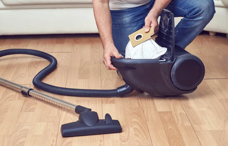 man taking out a full dust bag from a vacuum cleaner
