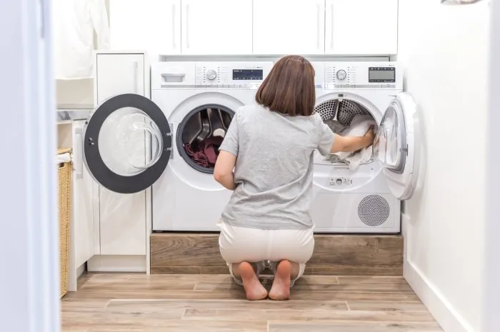 woman loading dirty clothes in washing machine for washing in modern utility room