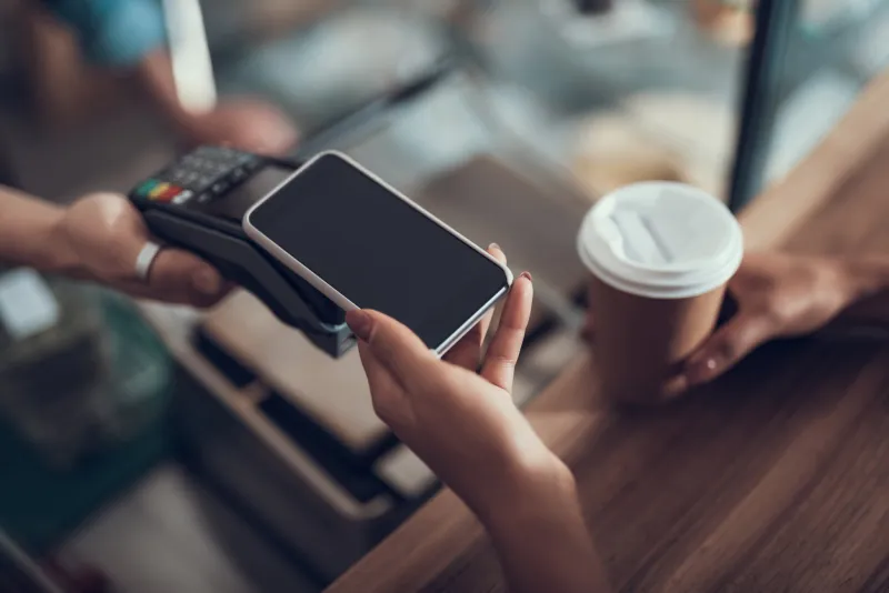 careful progressive lady with manicure holding her smartphone over the credit card payment machine while using contactless payment system