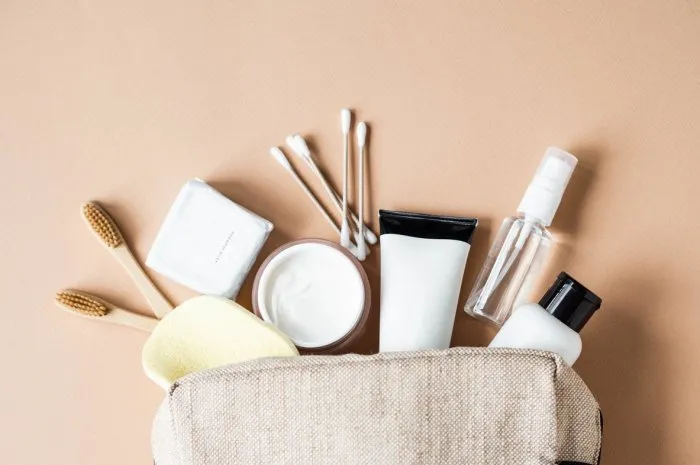 travel cosmetic bag with the necessary means to care for women's skin cosmetics, dry shampoo, cotton buds, toothbrushes next a cosmetic bag on a beige background top view