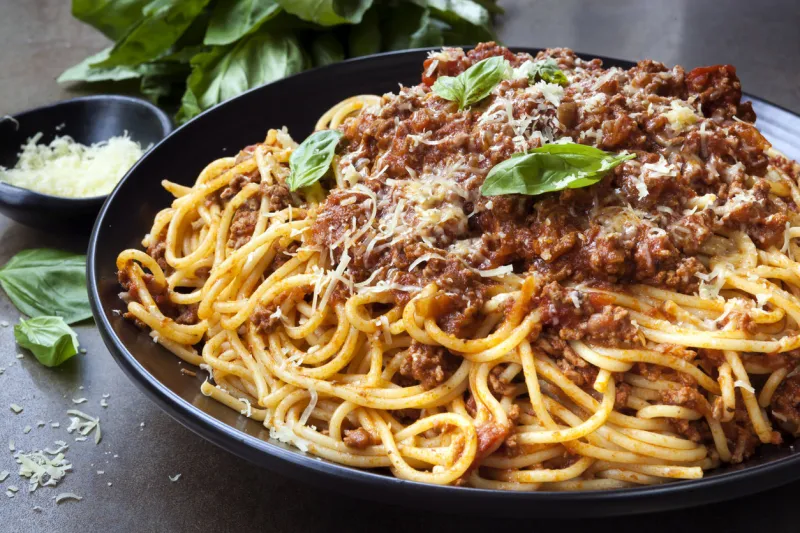 spaghetti bolognese in black serving platter, with fresh basil and parmesan