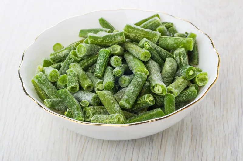 frozen green beans in white bowl on wooden table