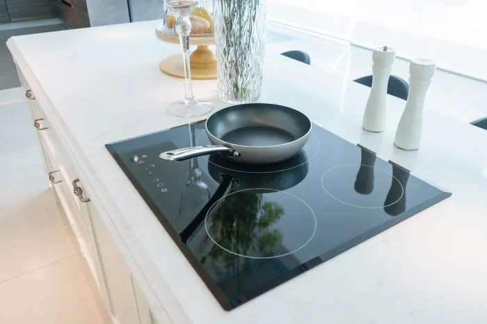 frying pan on modern black induction stove, cooker, hob or built in cooktop with ceramic top in white kitchen interior
