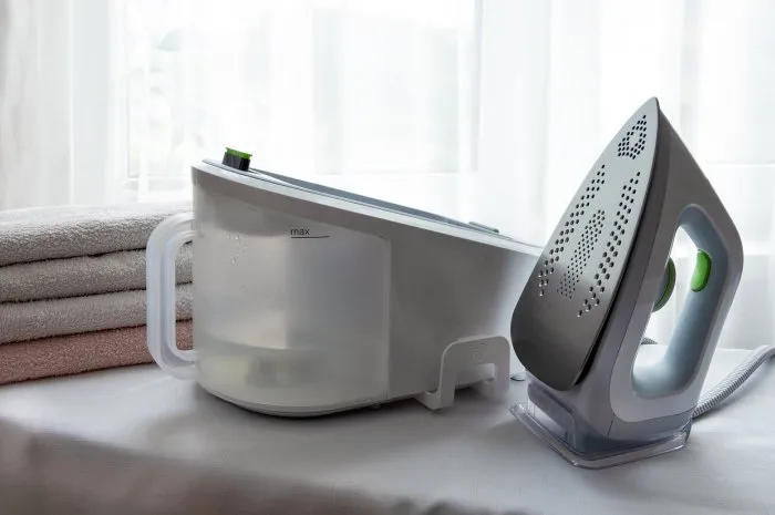 an electric iron with a steam generator and a stack of ironed towels on a light surface economics, ironing underwear horizontal orientation, selective focus