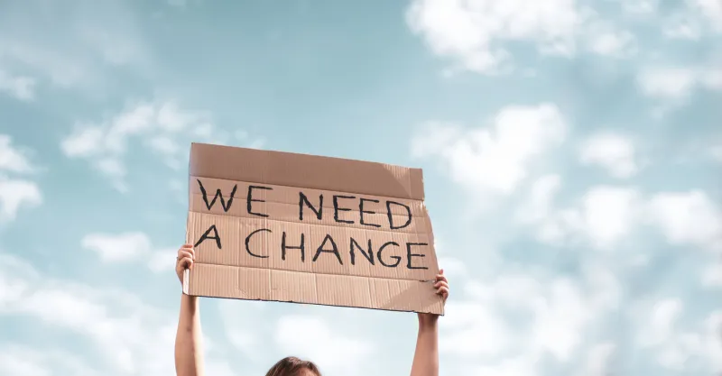 woman holding a banner of 'we need a change' young woman with poster in front of people protesting about climate changing on the street meeting about problem in ecology, environment, global warming, industrial influence, climate emergency